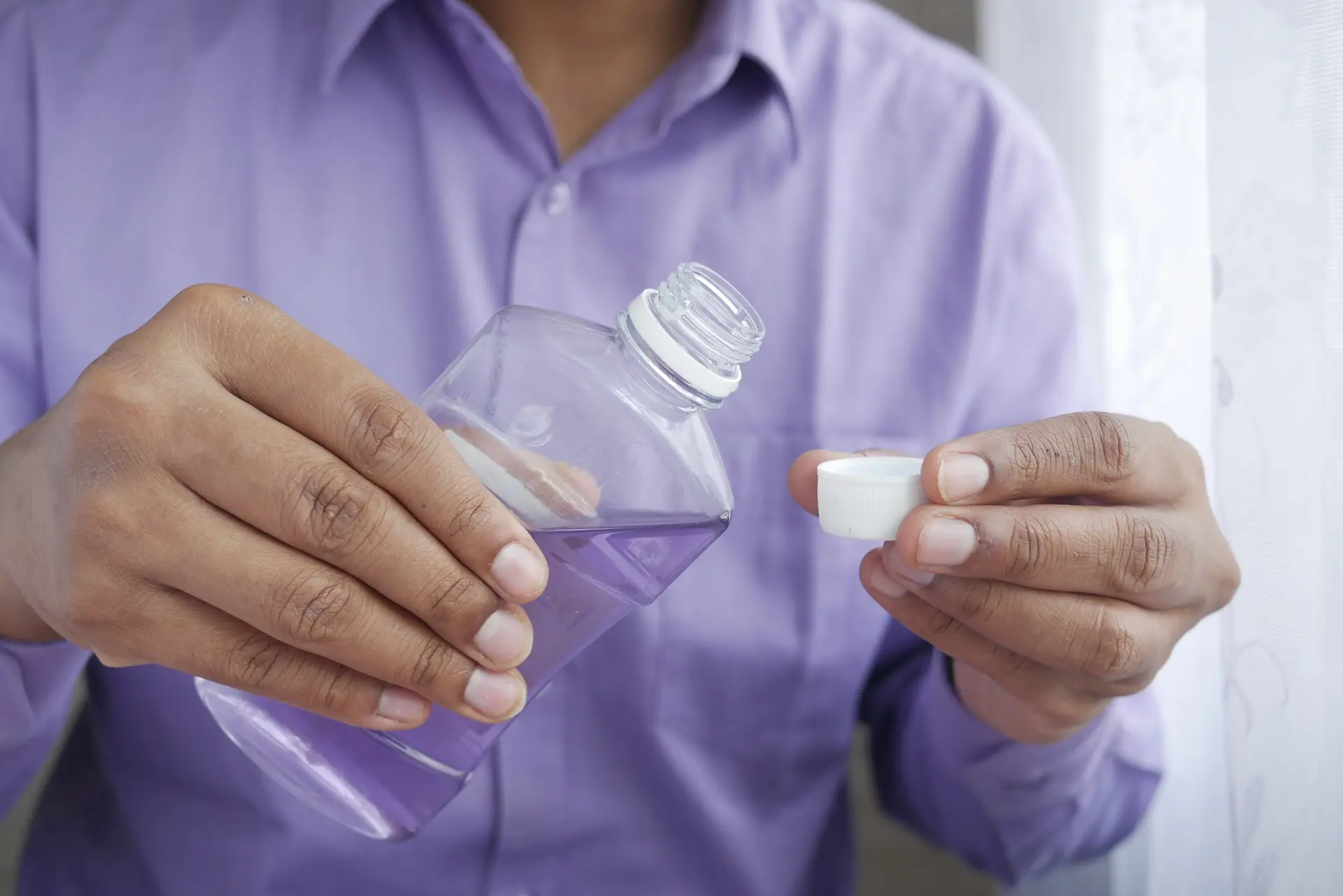 person in purple shirt holding mouthwash bottle and cap