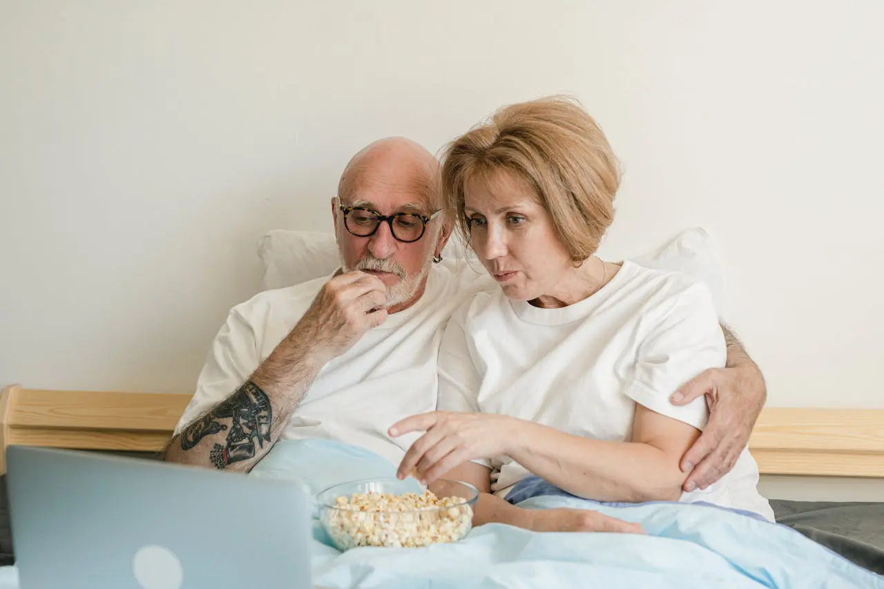 older couple eating popcorn while laying in bed