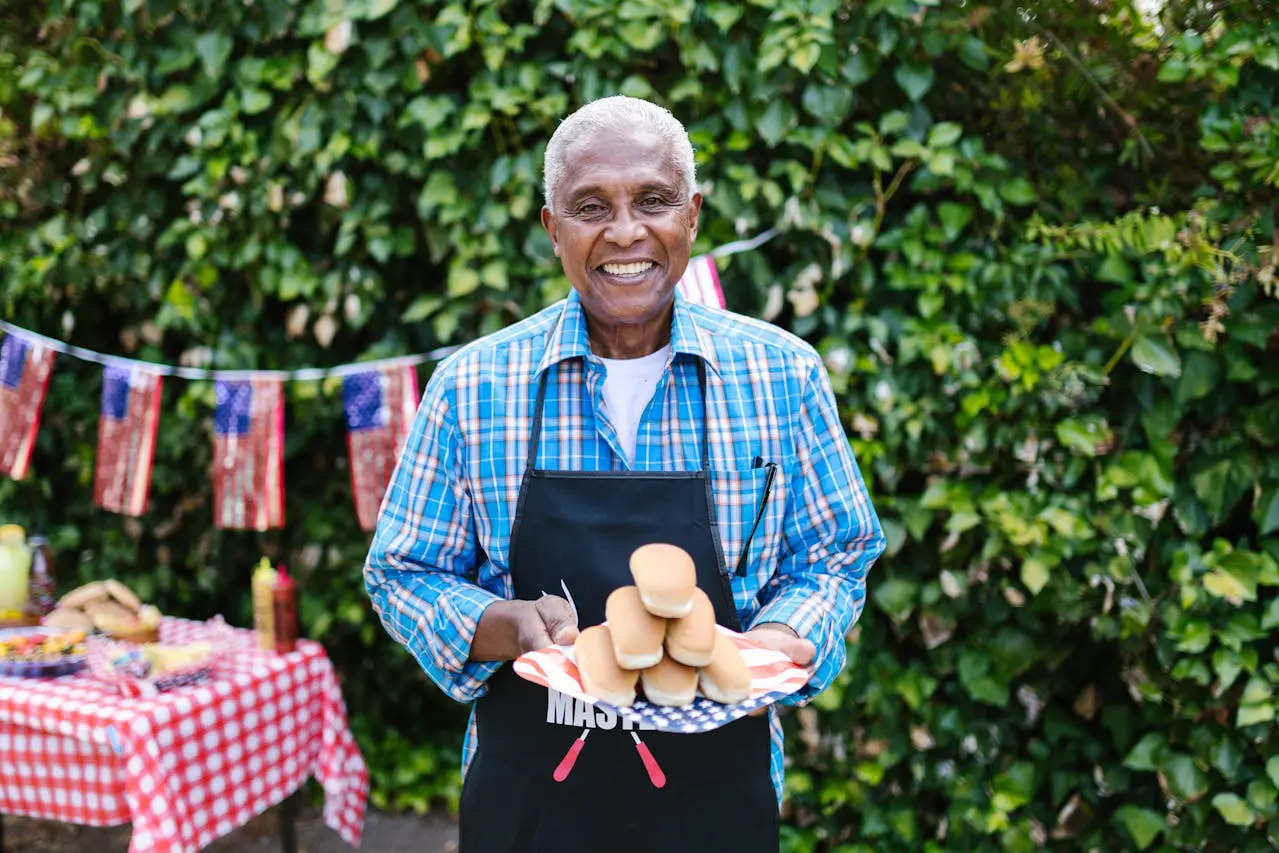 senior man smiling holding a plate of hot dogs in summer