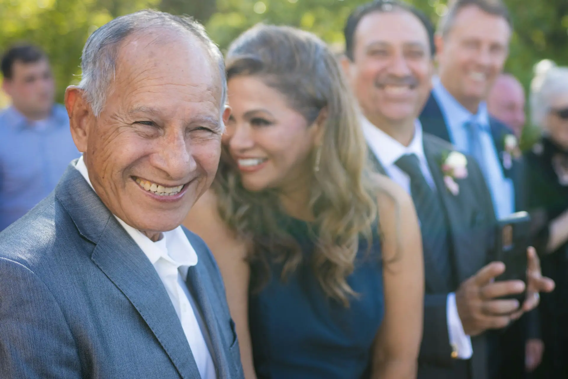 older man dressed in formal clothes and smiling with family around him