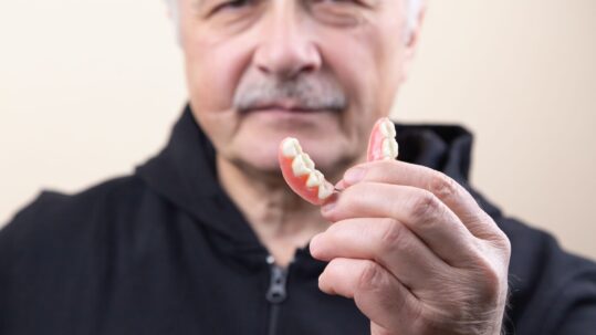 myths about dentures - man holding dentures in front of face