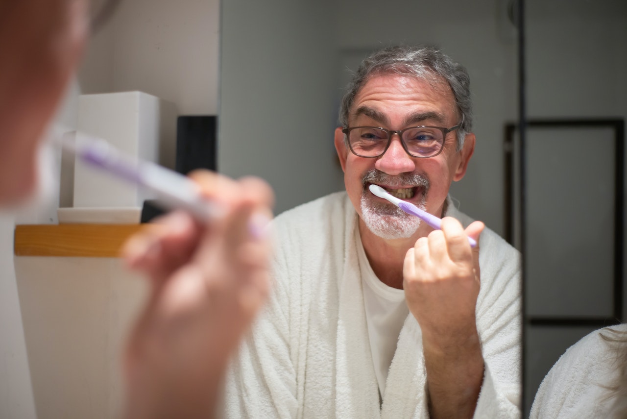 older man looking in mirror brushing teeth