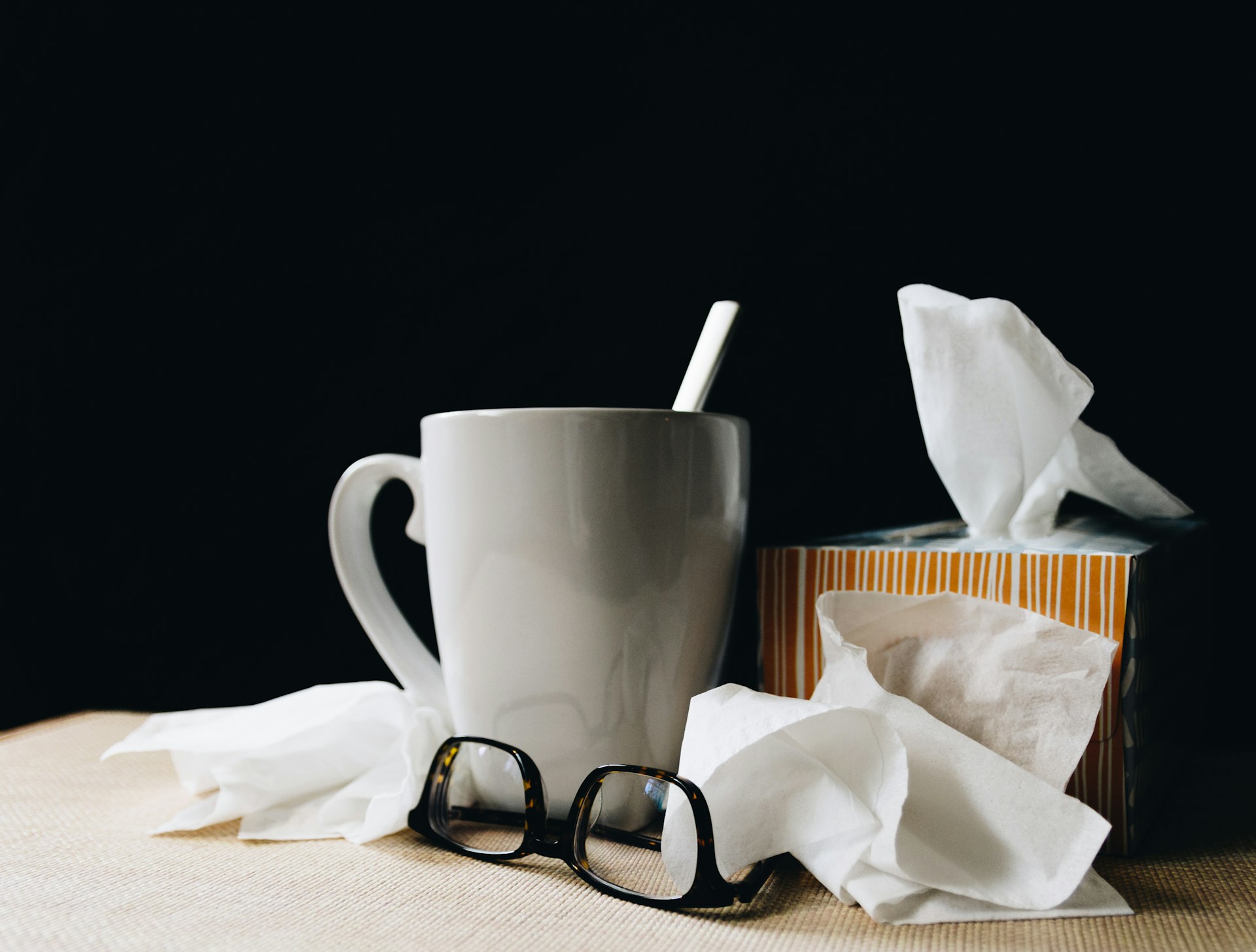 mug of tea, box of tissues, and reading glasses gathered on table