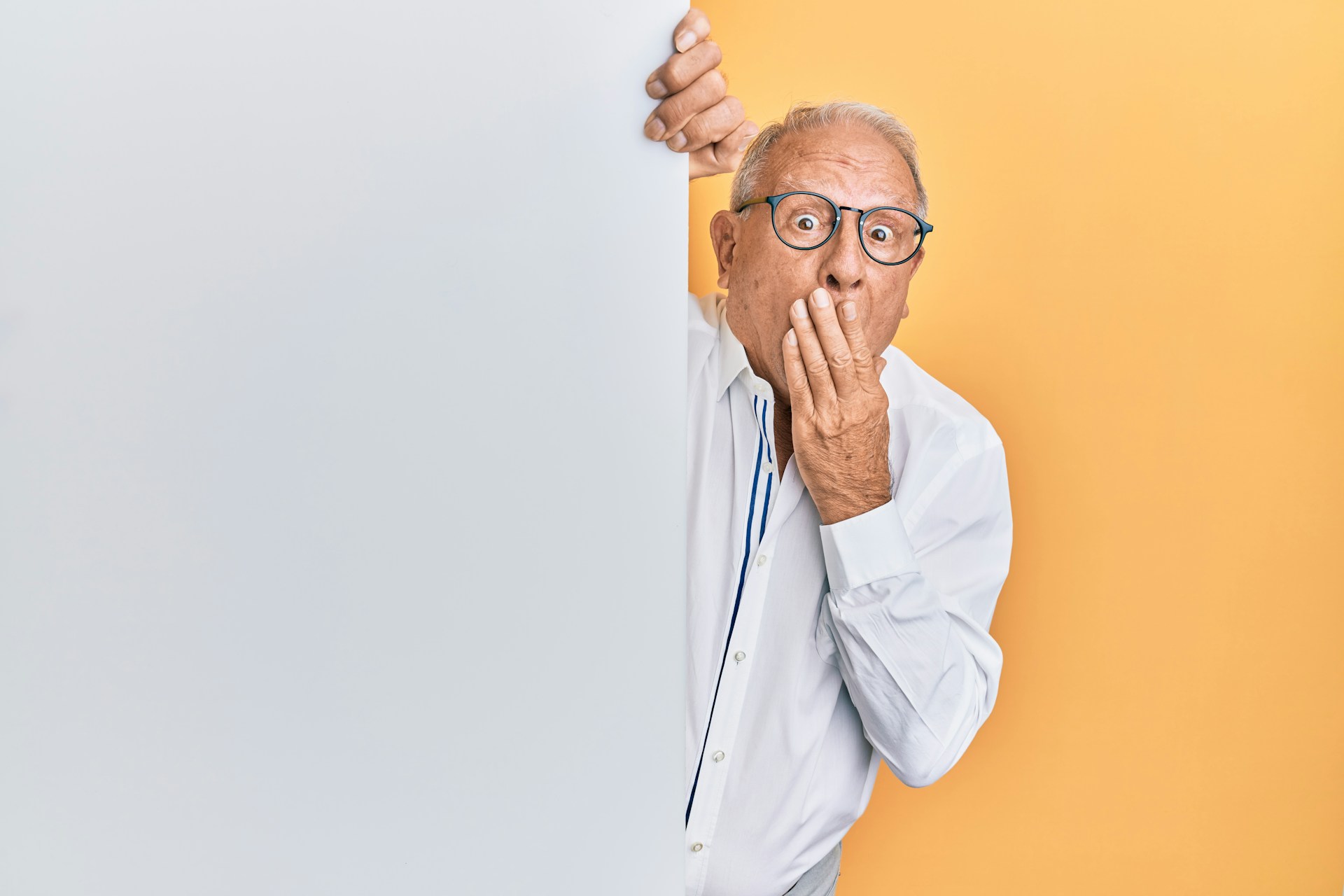 older man peeking around corner and covering mouth in surprise
